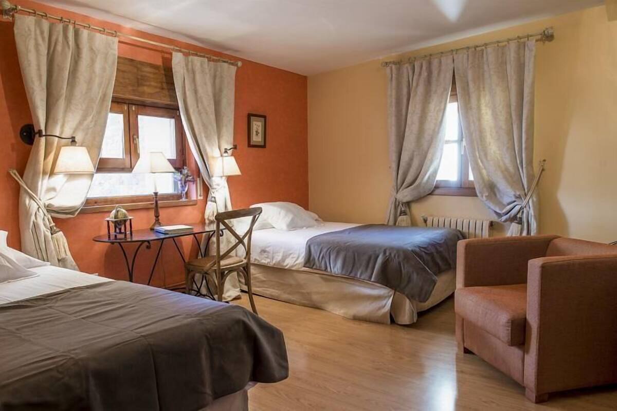 A room with two beds, a chair, a table, and a window with curtains.