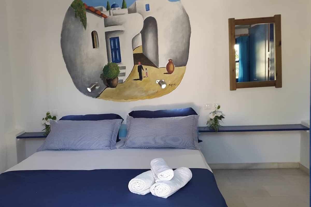 A bedroom with a bed, pillows, a wall mural, a mirror, and a nightstand with a plant.