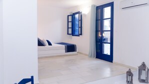 Una habitació amb un llit, una cadira, un taulell amb una ampolla i una finestra amb persianes blaves.
