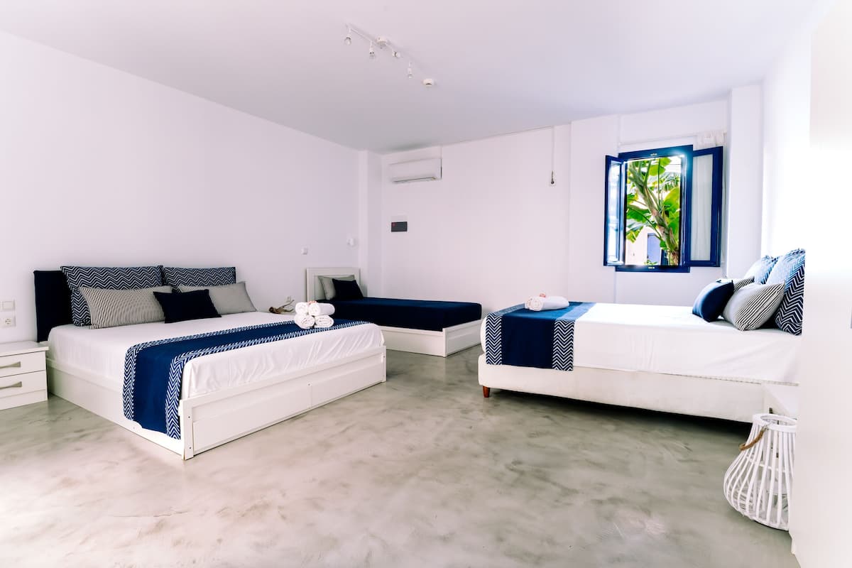A modern bedroom with two beds, a small table, and a window with a view of greenery.