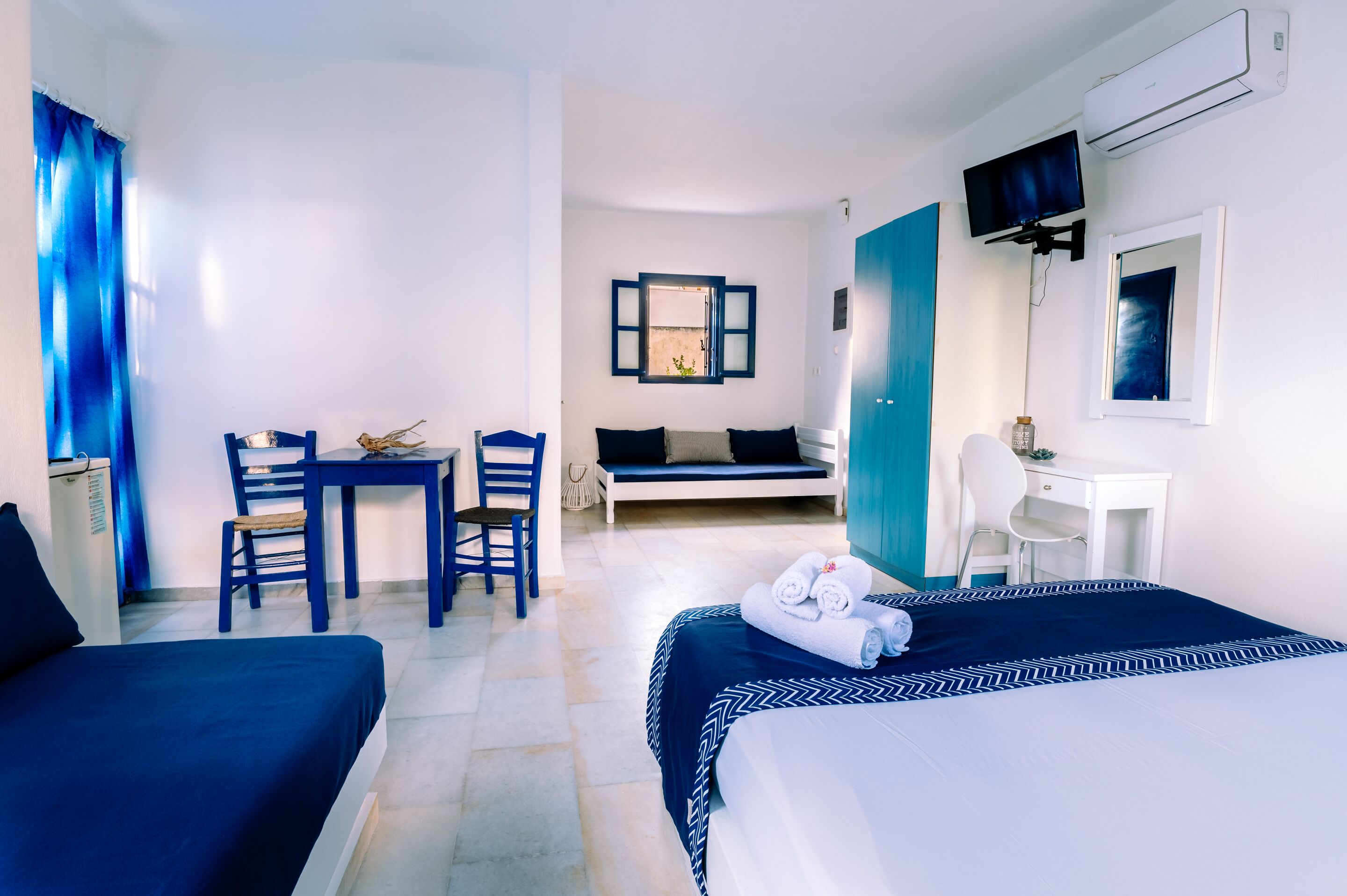 A hotel room with a bed, a desk, a chair, a sofa, and a TV.