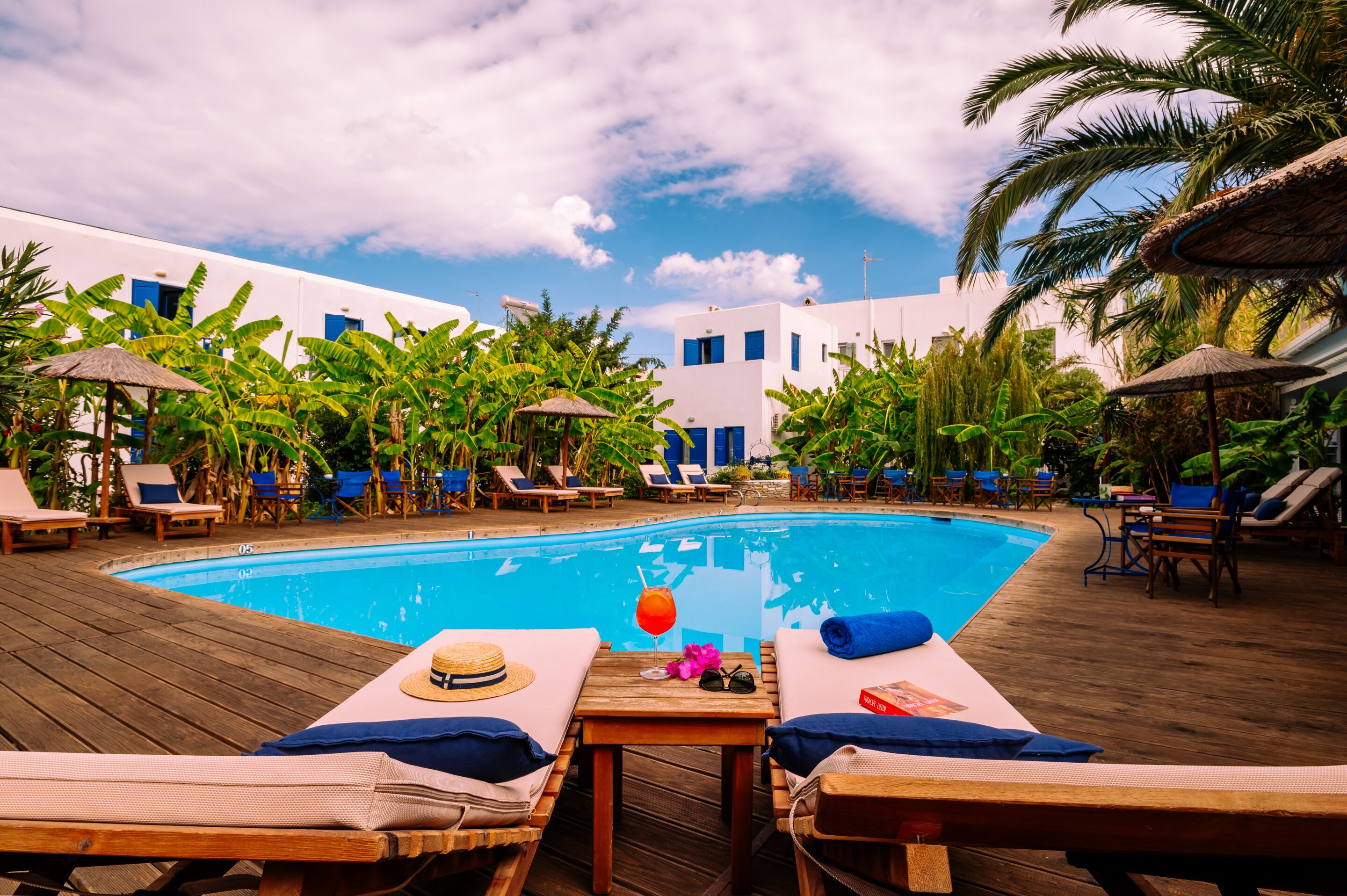 Un área al lado de la piscina con sillones de descanso, una terraza de madera y una piscina azul cristalina.