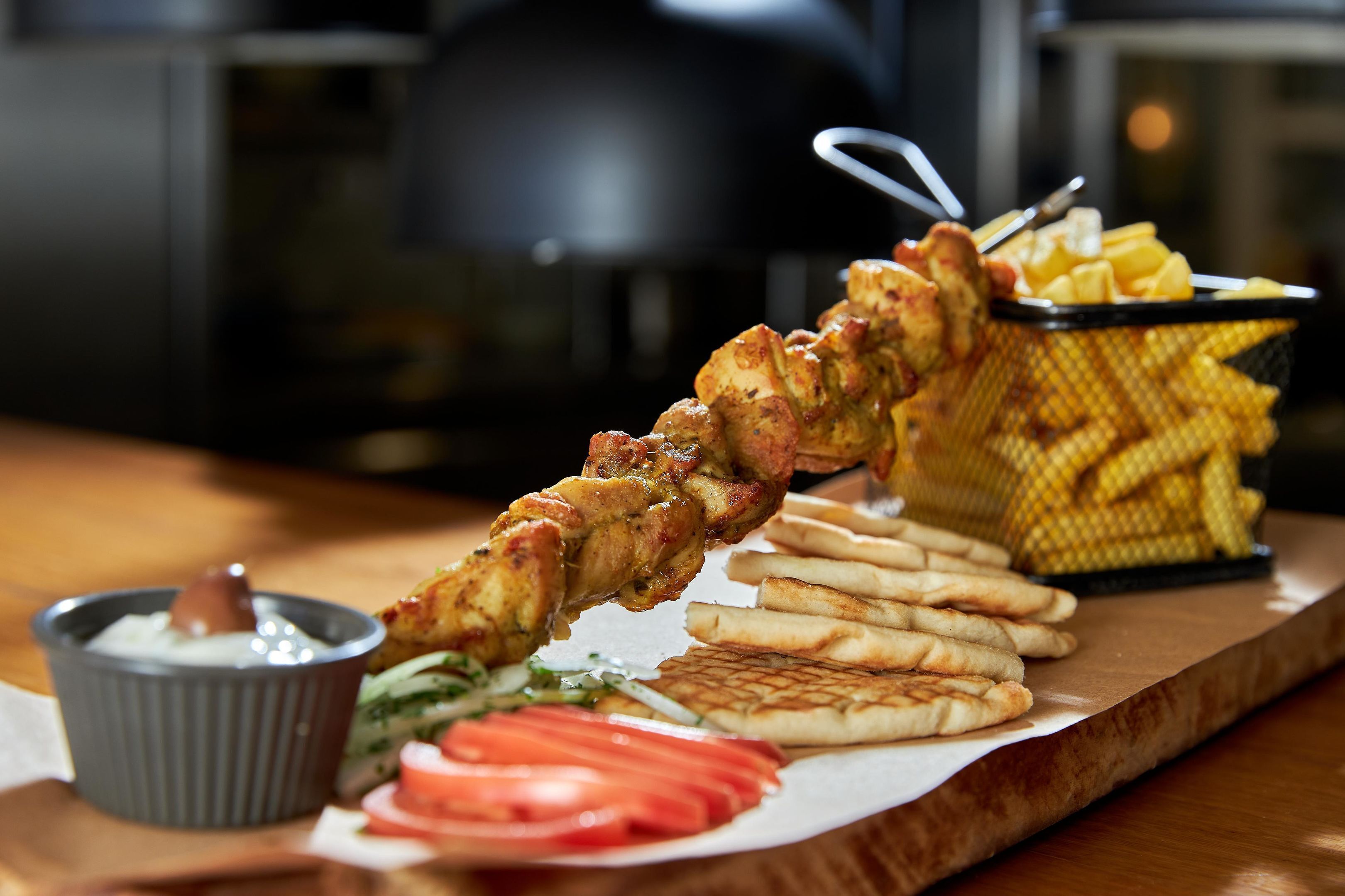 Un repas composé de poulet grillé, de frites et de pain pita, le tout servi sur une planche en bois.