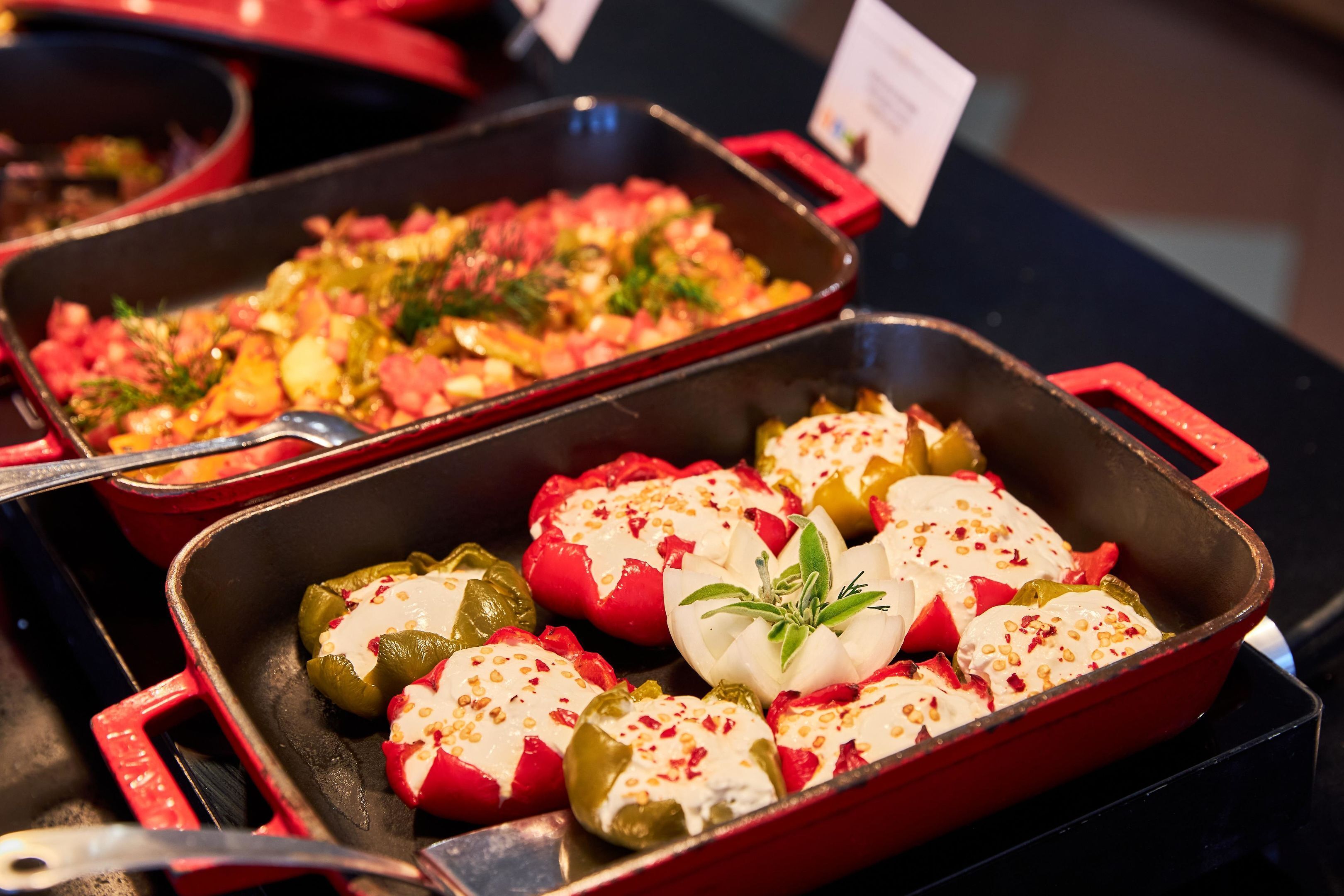 A kitchen with two red baking pans, one containing stuffed bell peppers and the other containing a vegetable dish.