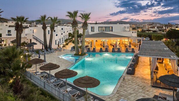 Una piscina sul tetto con lettini e ombrelloni, circondata da palme e edifici moderni.