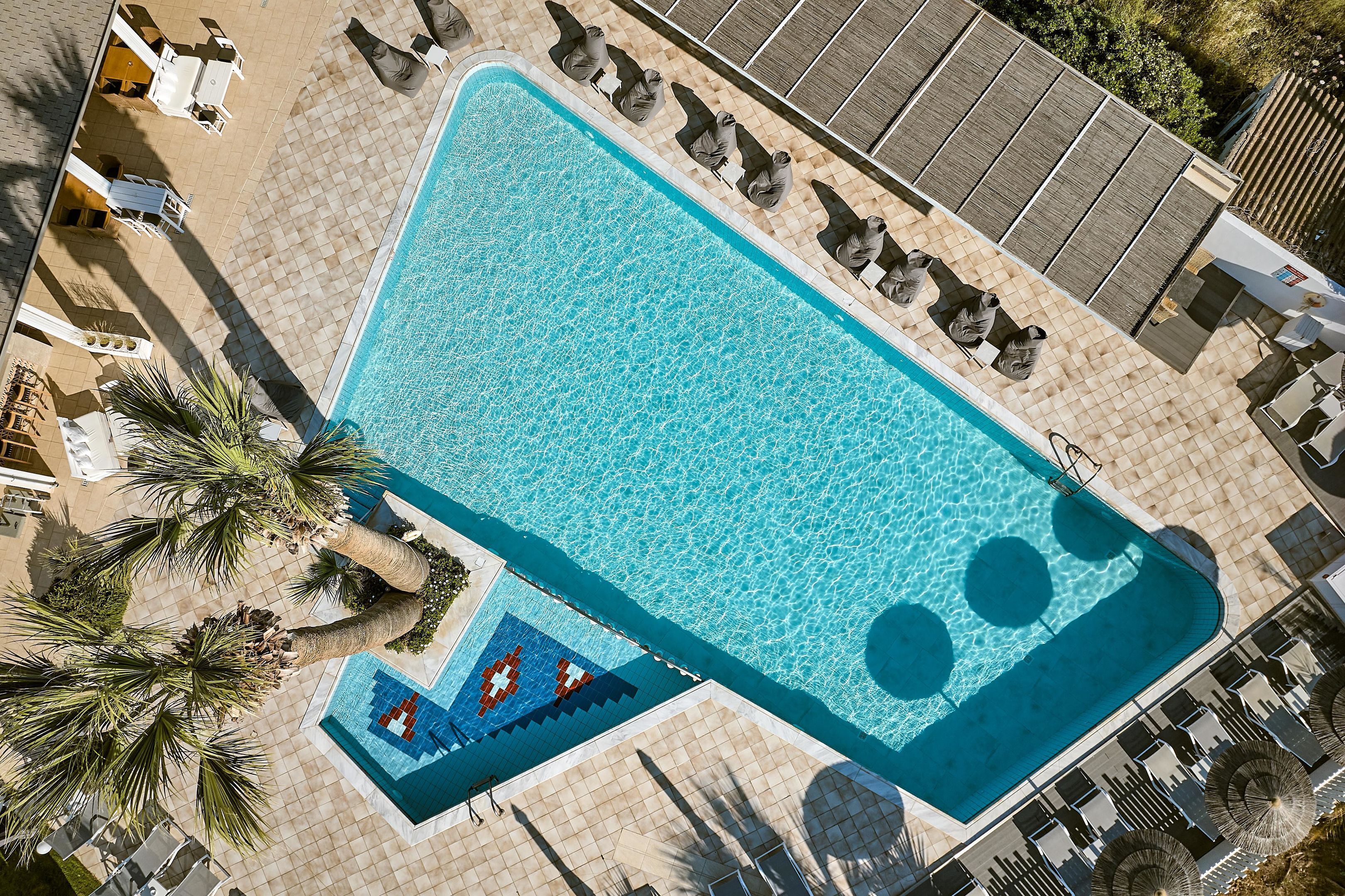 A rectangular swimming pool with a tiled deck, surrounded by lounge chairs and umbrellas.