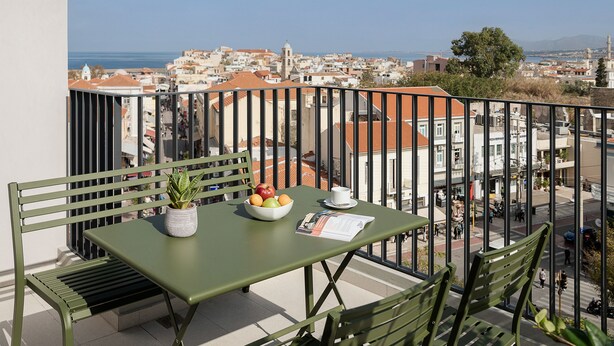 A balcony with a table, chairs, a bowl of fruit, a potted plant, and a menu. - Arkadi Hotel (Chania)