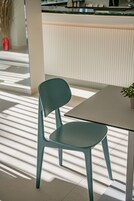 A teal chair and table in a modern, sunlit room with a tiled floor and a white wall.