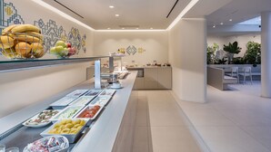 A modern buffet setup with various food items and a seating area with chairs and a table. - Arkadi Hotel (Chania)