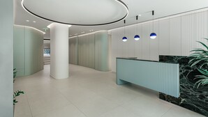 A modern reception area with a circular light fixture, a reception desk, and a plant. - Arkadi Hotel (Chania)