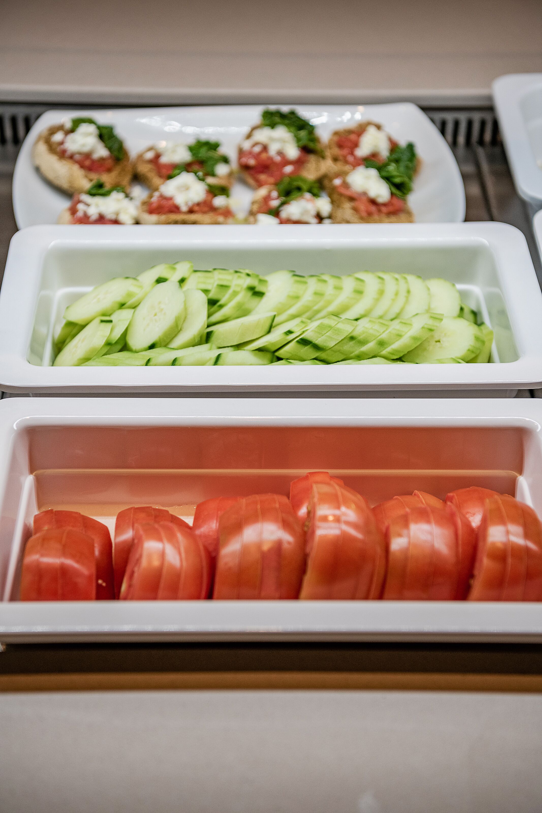 A buffet with sliced cucumbers, tomatoes, and a plate of bruschetta.