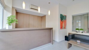 A modern reception area with a wooden counter, a black sofa, and a large mirror. - Marirena (Malevizi)