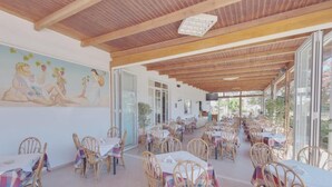 An outdoor dining area with wicker chairs and tables, a mural on the wall, and a wooden ceiling. - Marirena (Malevizi)