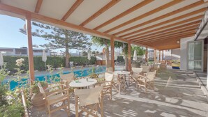 An outdoor patio area with wooden tables and chairs, a pool, and a covered seating area. - Marirena (Malevizi)