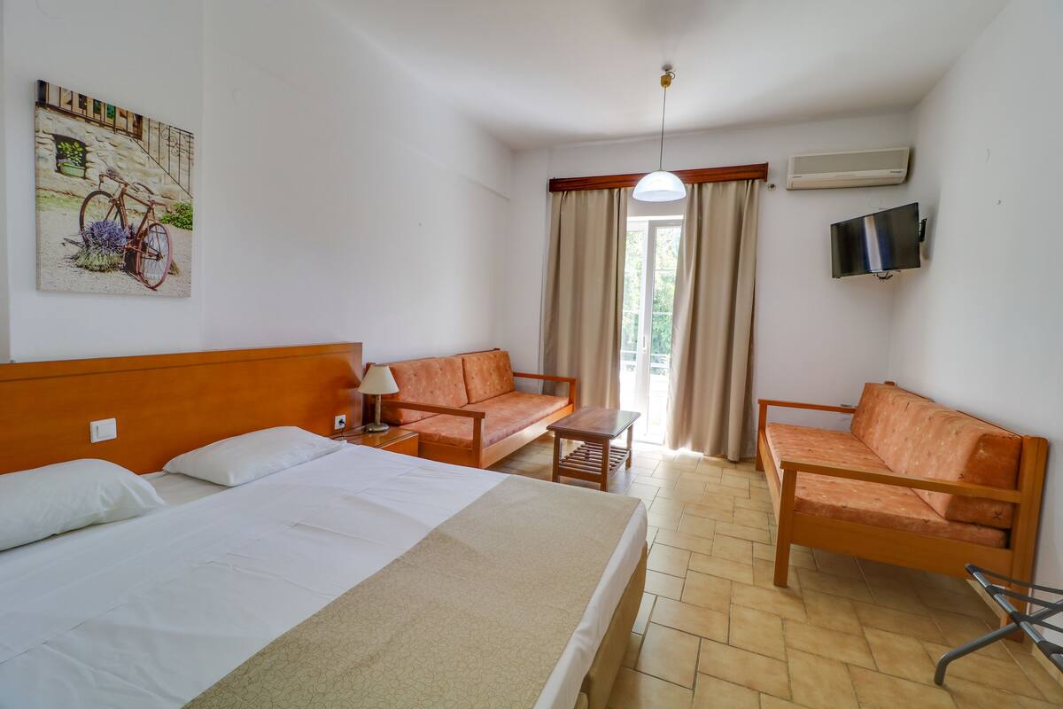 Habitación de hotel con cama, dos sofás, una mesita, televisor y ventana con cortinas.