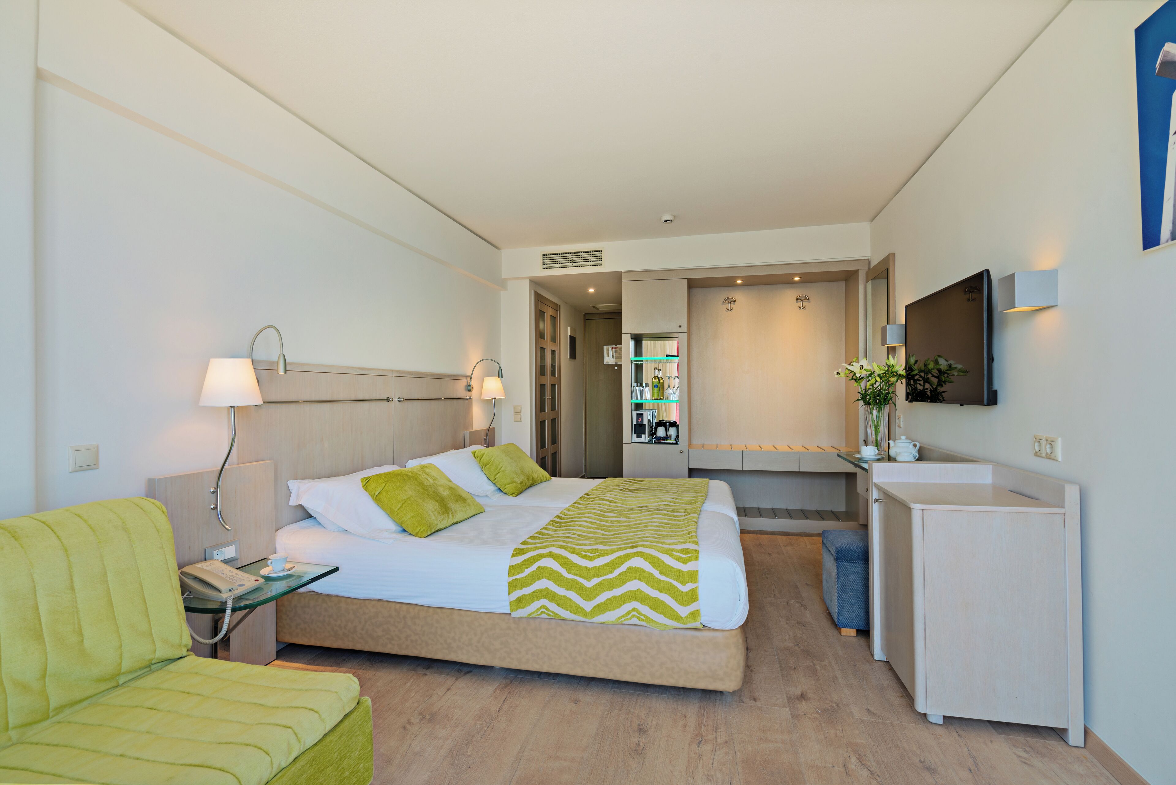 Habitación de hotel con cama, escritorio, silla, televisión y kitchenette pequeña.