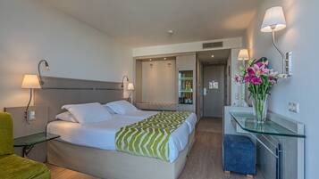 Una habitación de hotel moderna con cama, mesita de noche, lámpara y un pequeño escritorio con un florero.