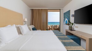 A hotel room with a large bed, a desk, a chair, a TV, and a view of the ocean. - Kriti Beach (Rethymno)