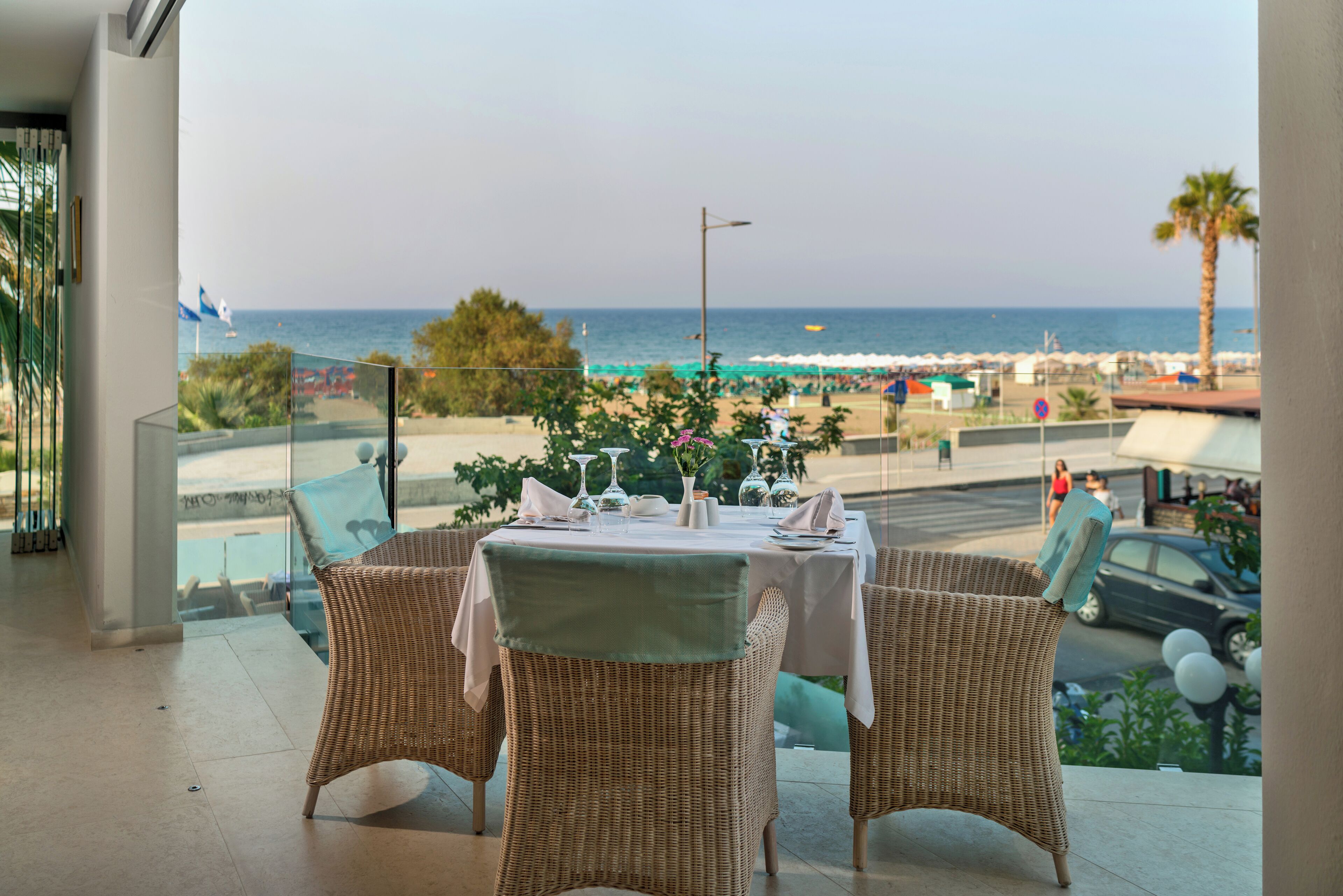 A dining area with wicker chairs and a table set for two, overlooking a beach and the sea.