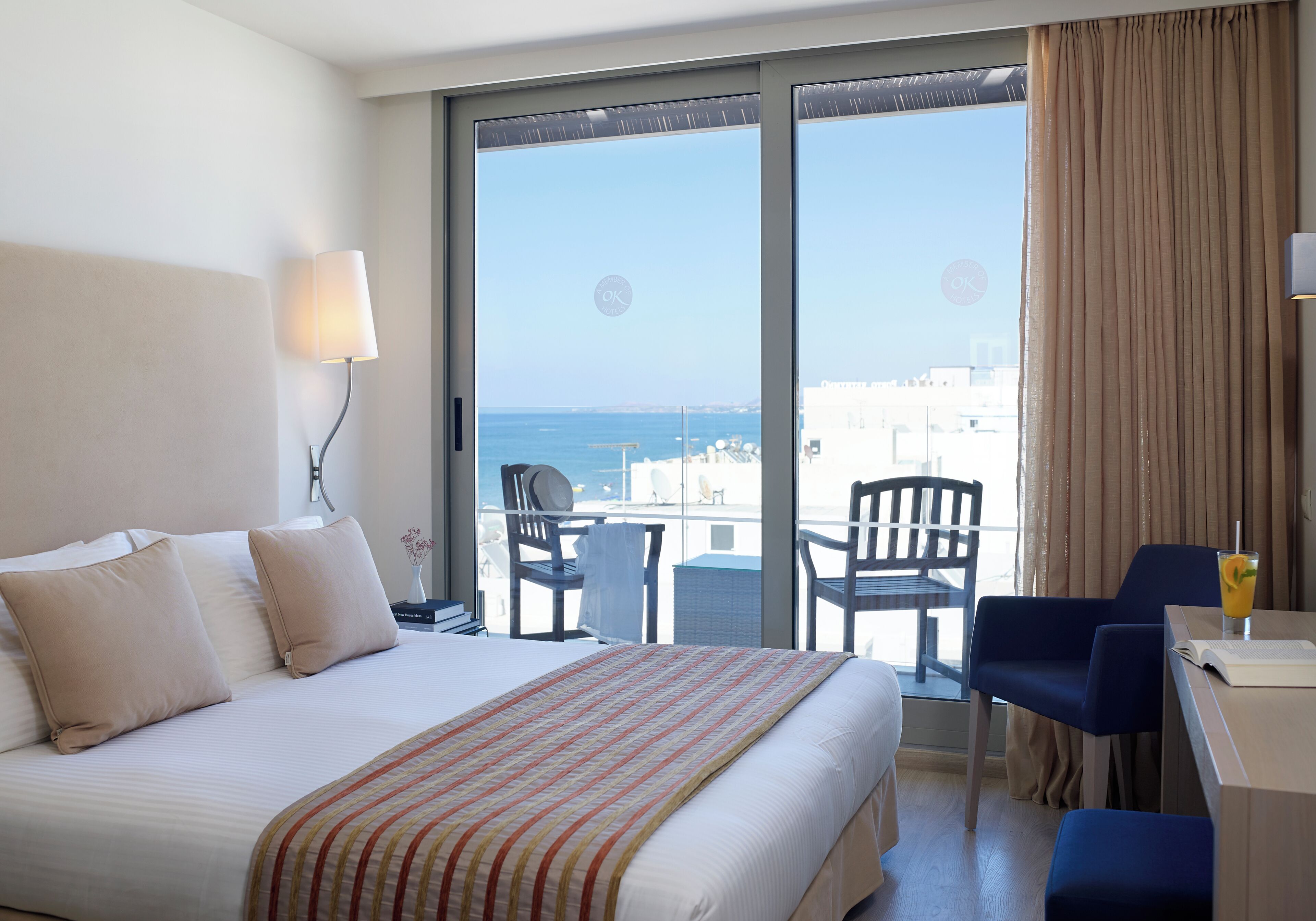 A hotel room with a bed, a desk, and a view of the sea.