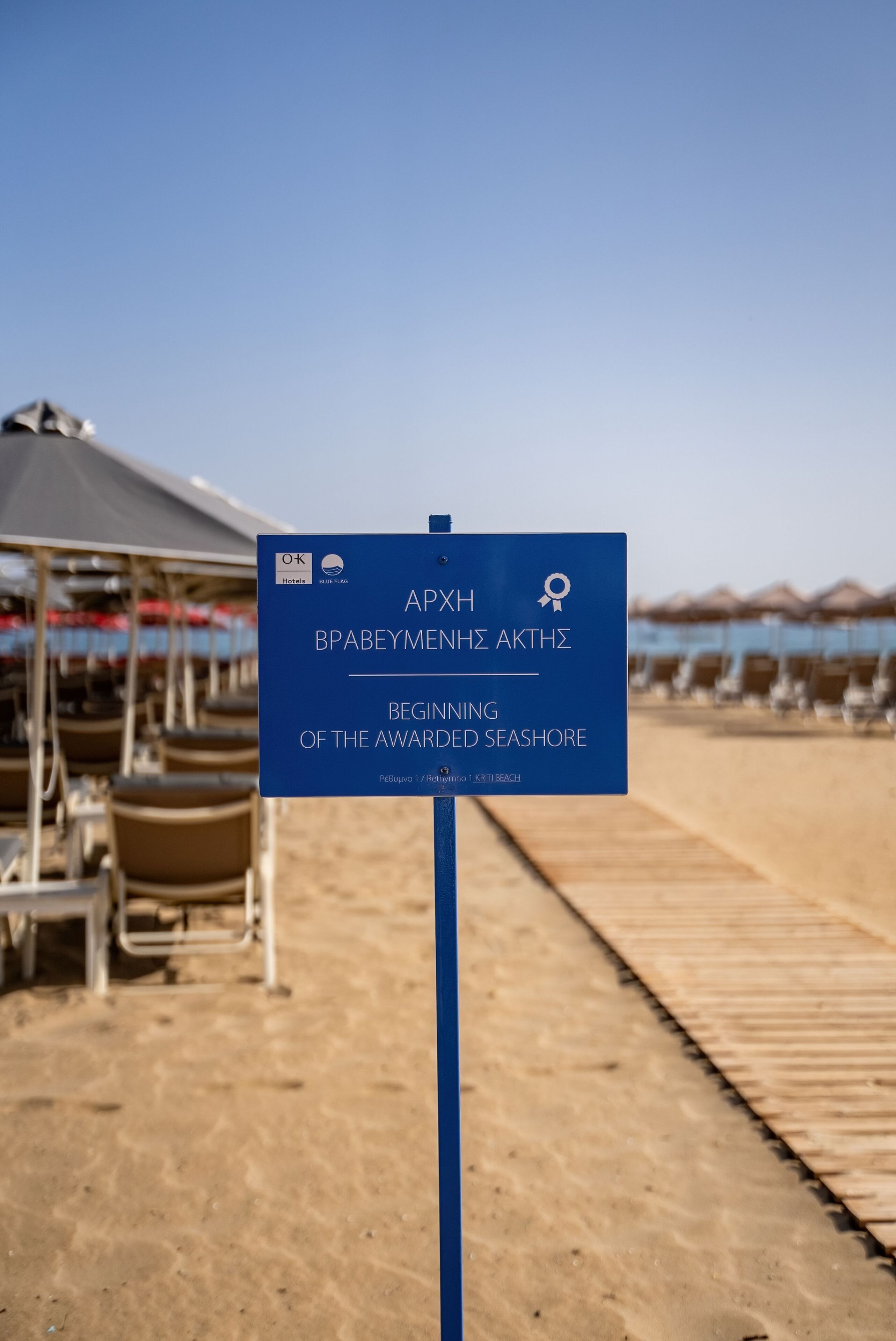 Een bord dat het begin van het bekroonde strand aangeeft, met een tent en strandstoelen op de achtergrond.