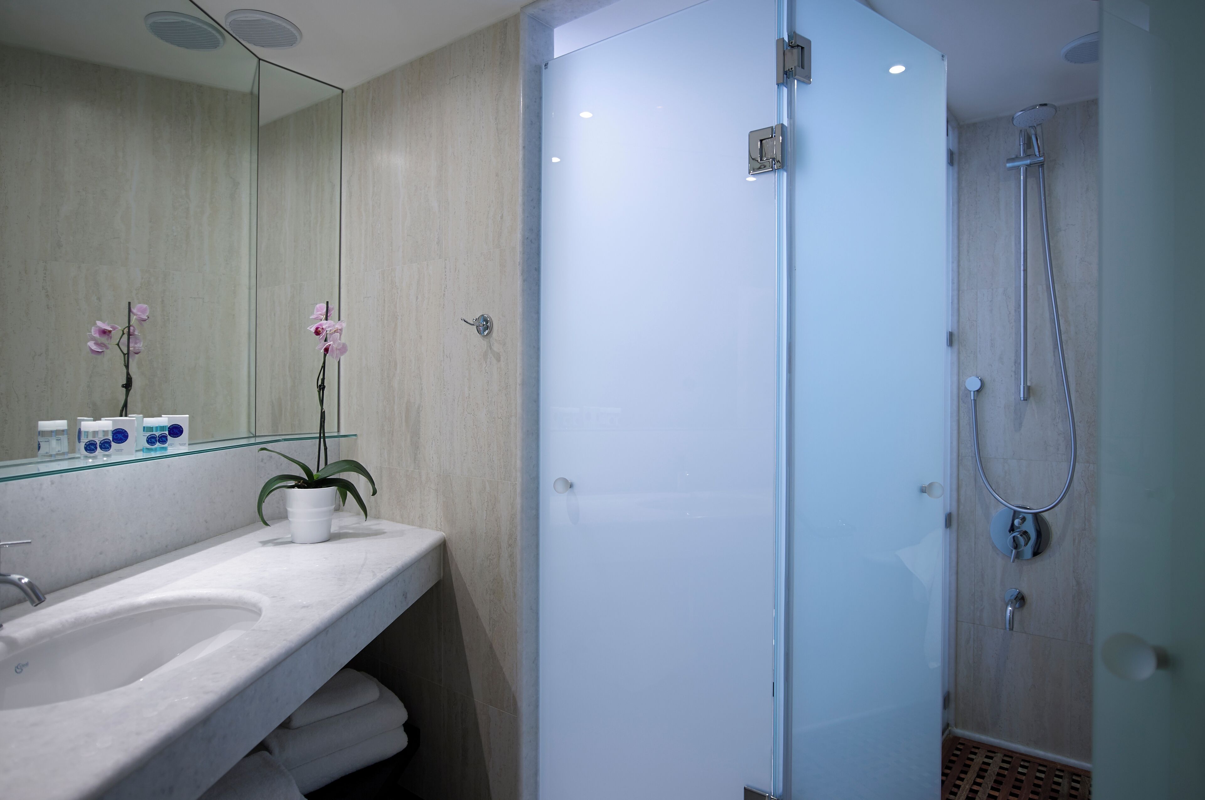 A modern bathroom with a glass-enclosed shower, a marble sink, and a mirror with orchids.
