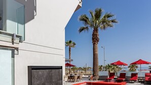 A modern pool area with red-tiled flooring, palm trees, and red umbrellas. - Kriti Beach (Rethymno)