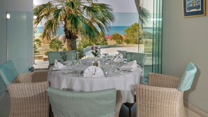 A dining area with a table set for four, overlooking a beach with palm trees and the ocean. - Kriti Beach (Rethymno)