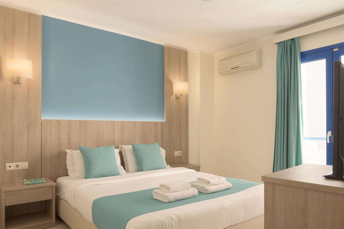 Ein Hotelzimmer mit Bett, Nachttischen, einem Schreibtisch und einem Vorhangfenster.