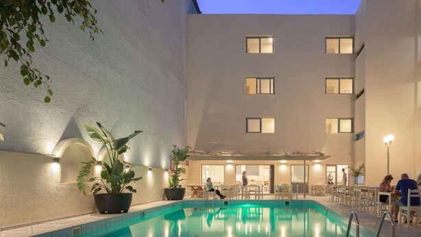Una piscina interior con borde de azulejos, rodeada por un edificio con varias ventanas y una zona de estar cubierta.