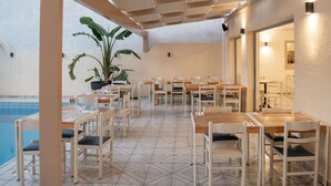 Un espacio de comedor al aire libre con mesas y sillas, una piscina y plantas en macetas.