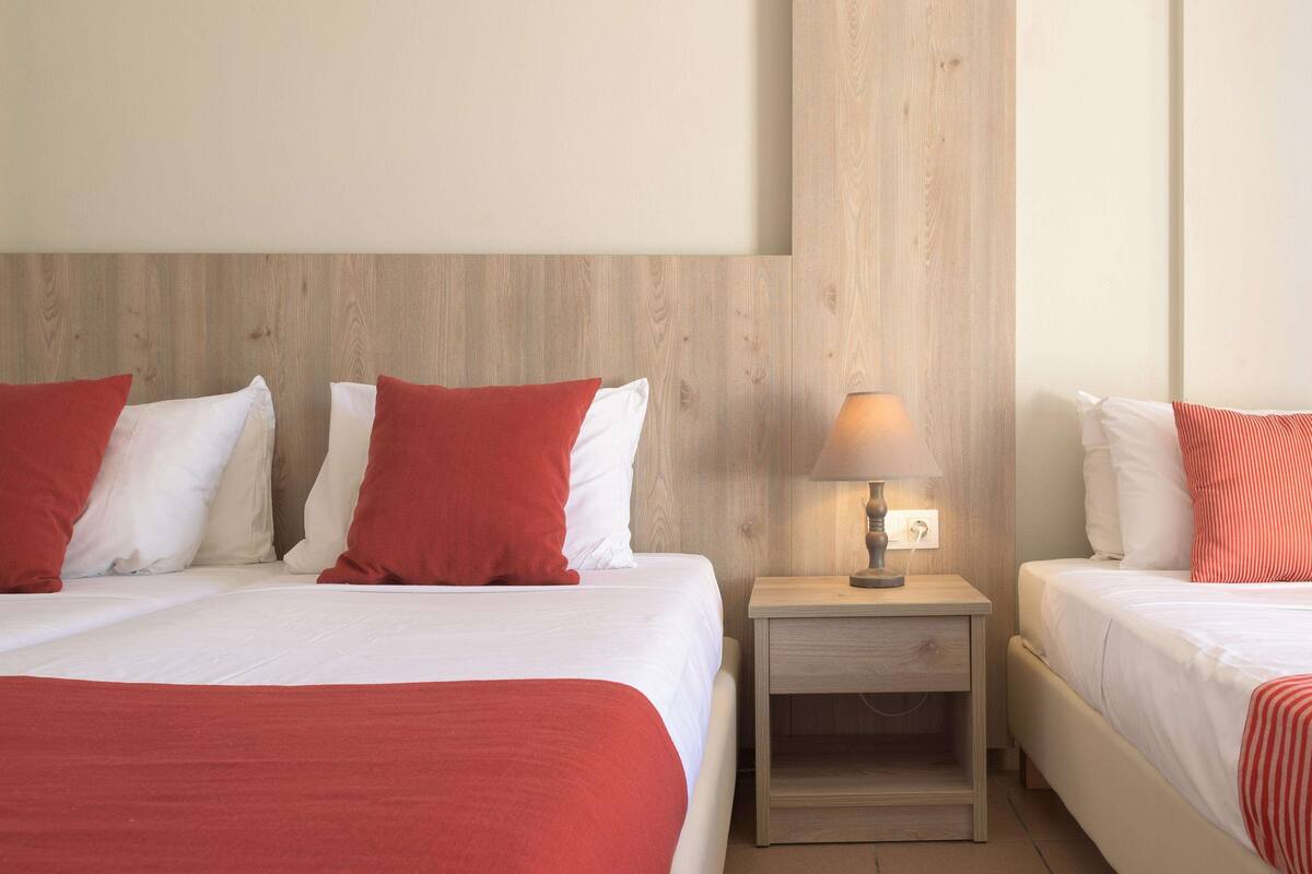 Ein Hotelzimmer mit zwei Betten, jeweils mit roter und weißer Bettwäsche, einem Holz-Kopfteil und einem Nachttisch mit Lampe.