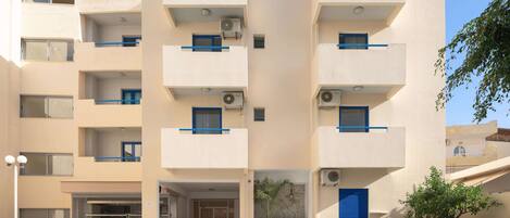 A multi-story hotel with a swimming pool, outdoor seating, and air conditioning units.