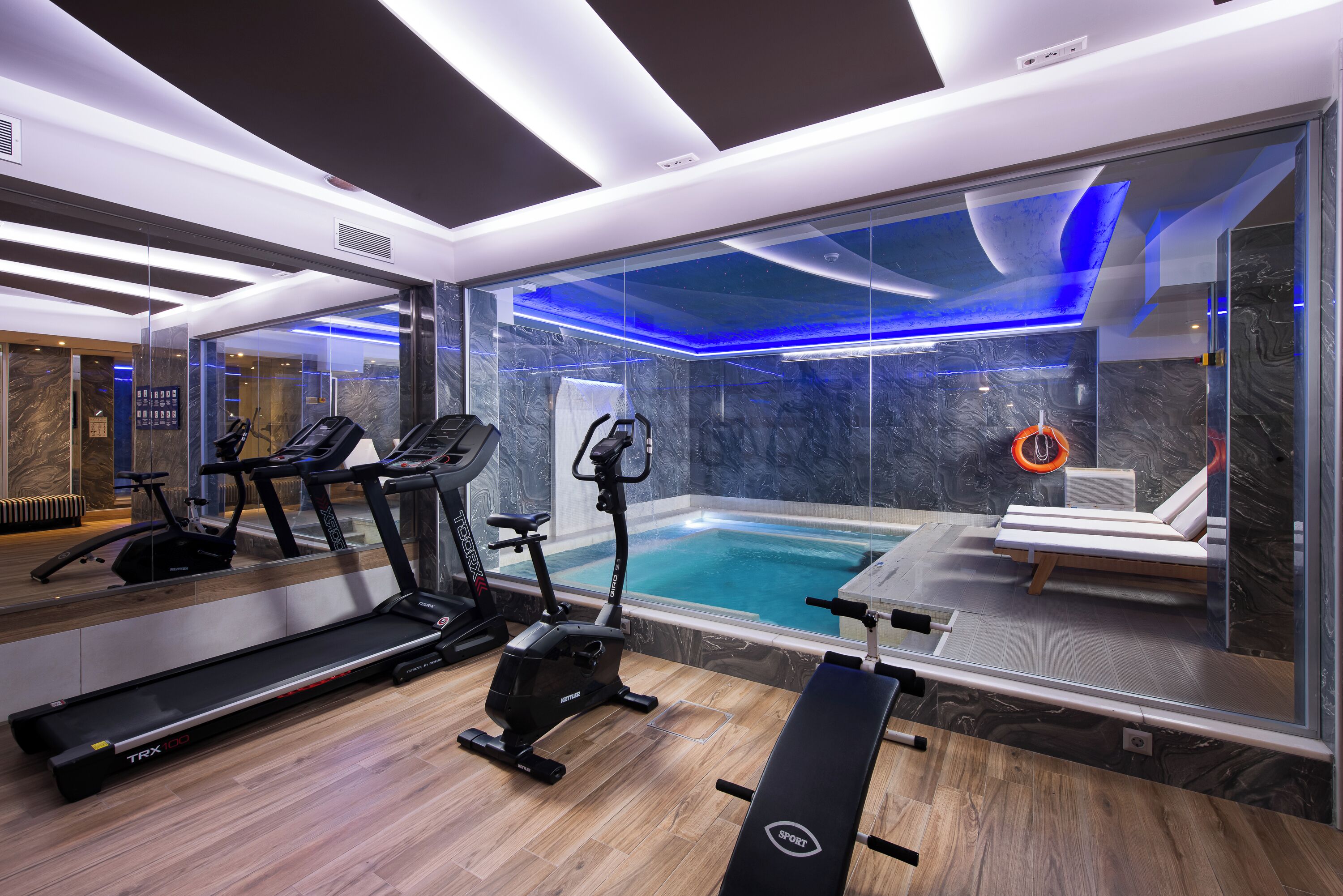Ett modernt gym med träningsutrustning, en stor spegel och utsikt över en simbassäng.