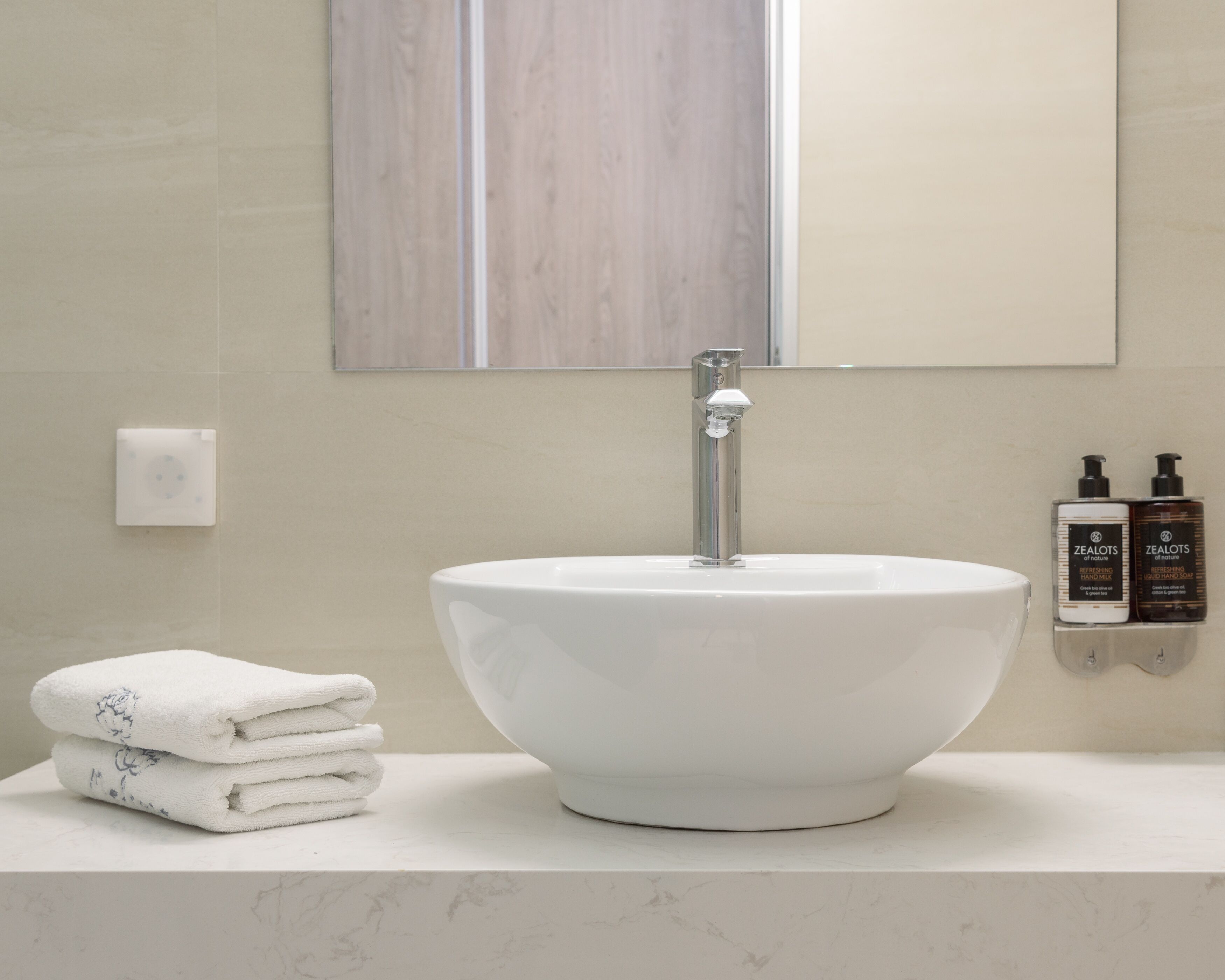 A bathroom with a white sink, a mirror, and two bottles of Zealots hand soap.