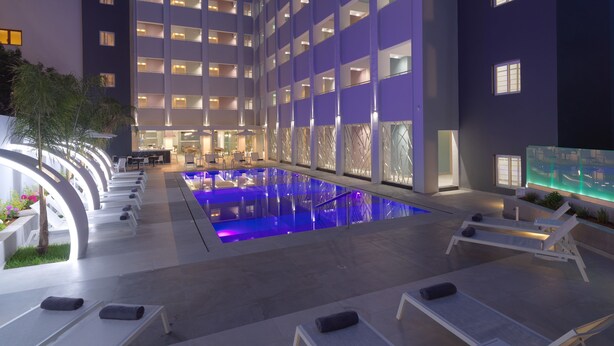 A hotel with a swimming pool, lounge chairs, and a modern building facade. - Melrose Rethymno by Mage Hotels (Rethymno)