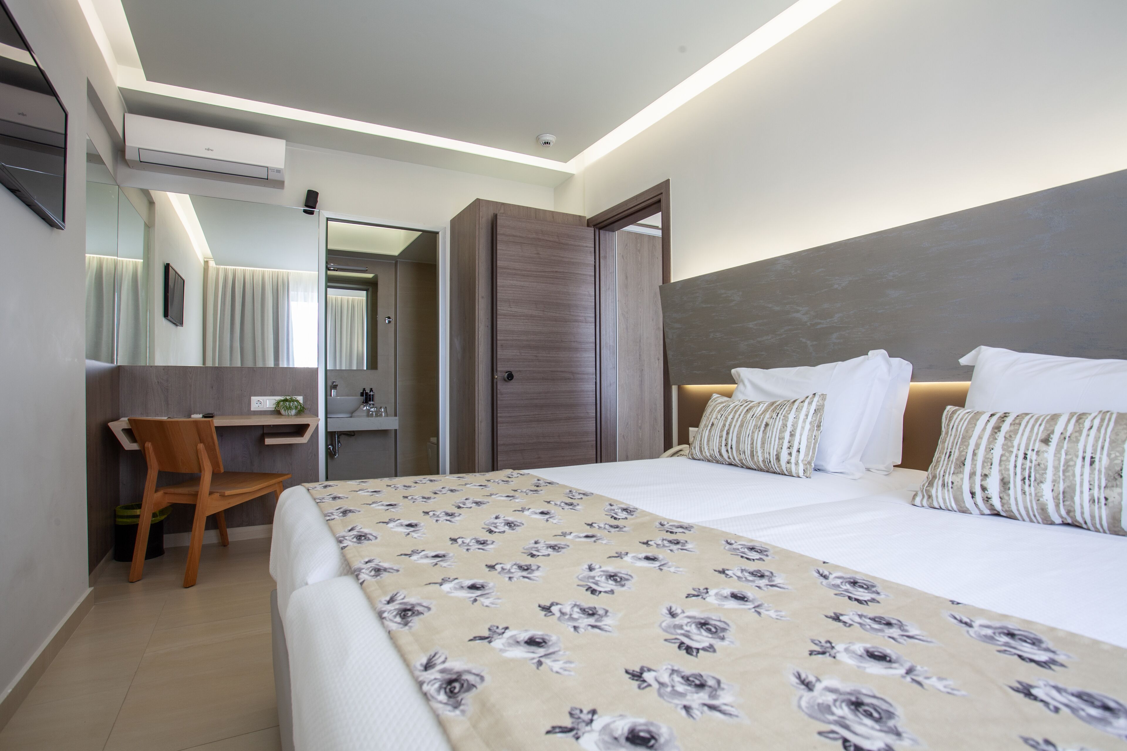 A hotel room with a bed, a desk, a chair, a mirror, and a wardrobe.