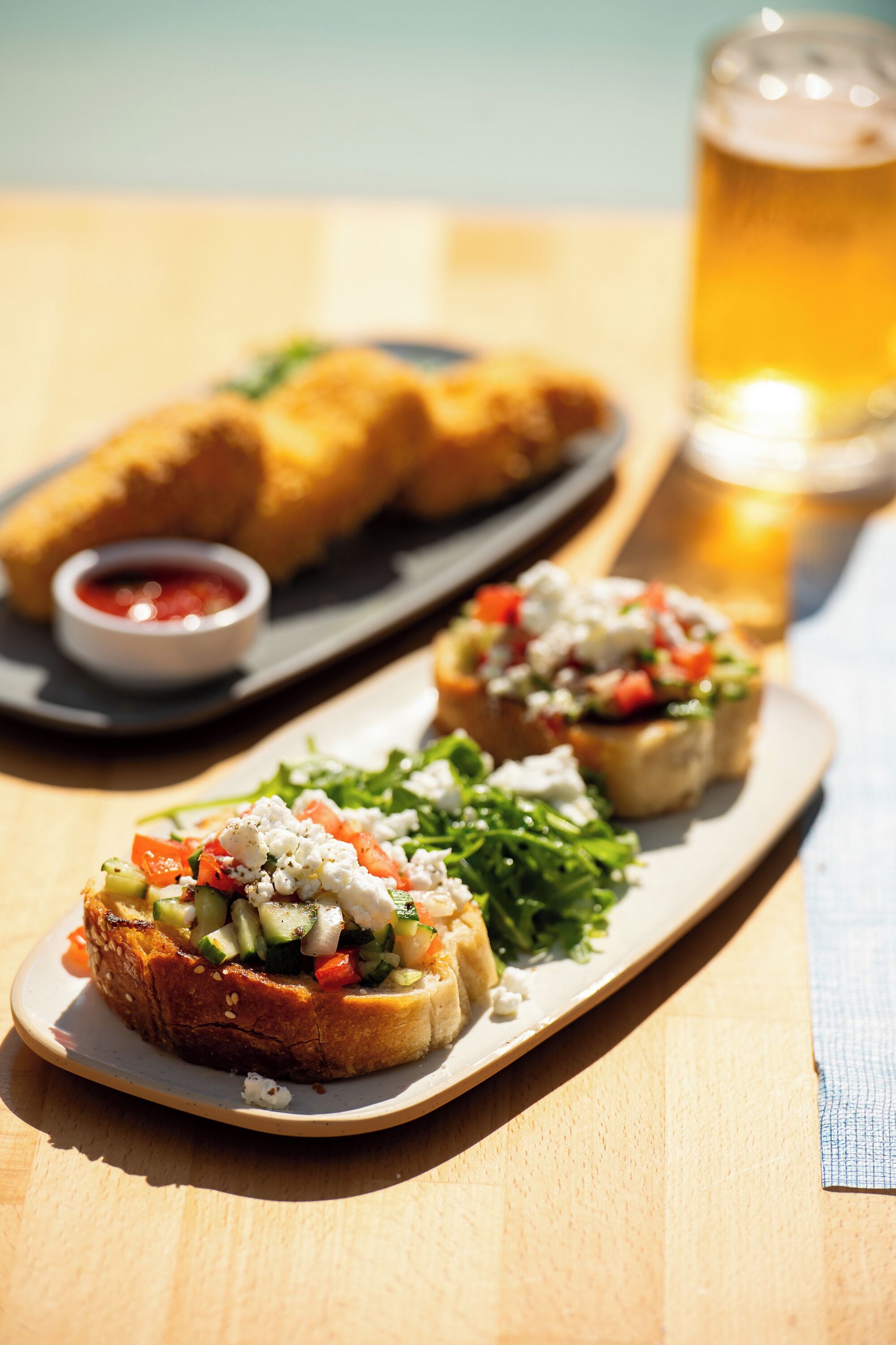 A wooden table with a plate of bruschetta and a glass of beer.