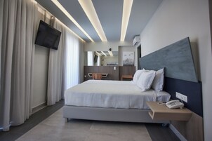 Una habitación de hotel moderna con una cama grande, una mesita de noche con un teléfono, un televisor de pantalla plana en la pared y un escritorio con una silla.