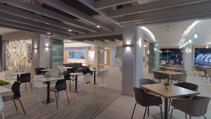 A modern indoor dining area with multiple tables and chairs, a visible kitchen area, and a glass partition separating the dining space from the kitchen. - Melrose Rethymno by Mage Hotels (Rethymno)