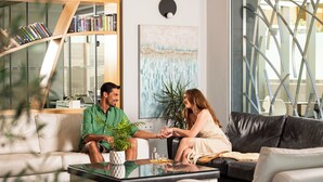 A modern living room with a glass coffee table, a sofa, and a bookshelf. - Melrose Rethymno by Mage Hotels (Rethymno)