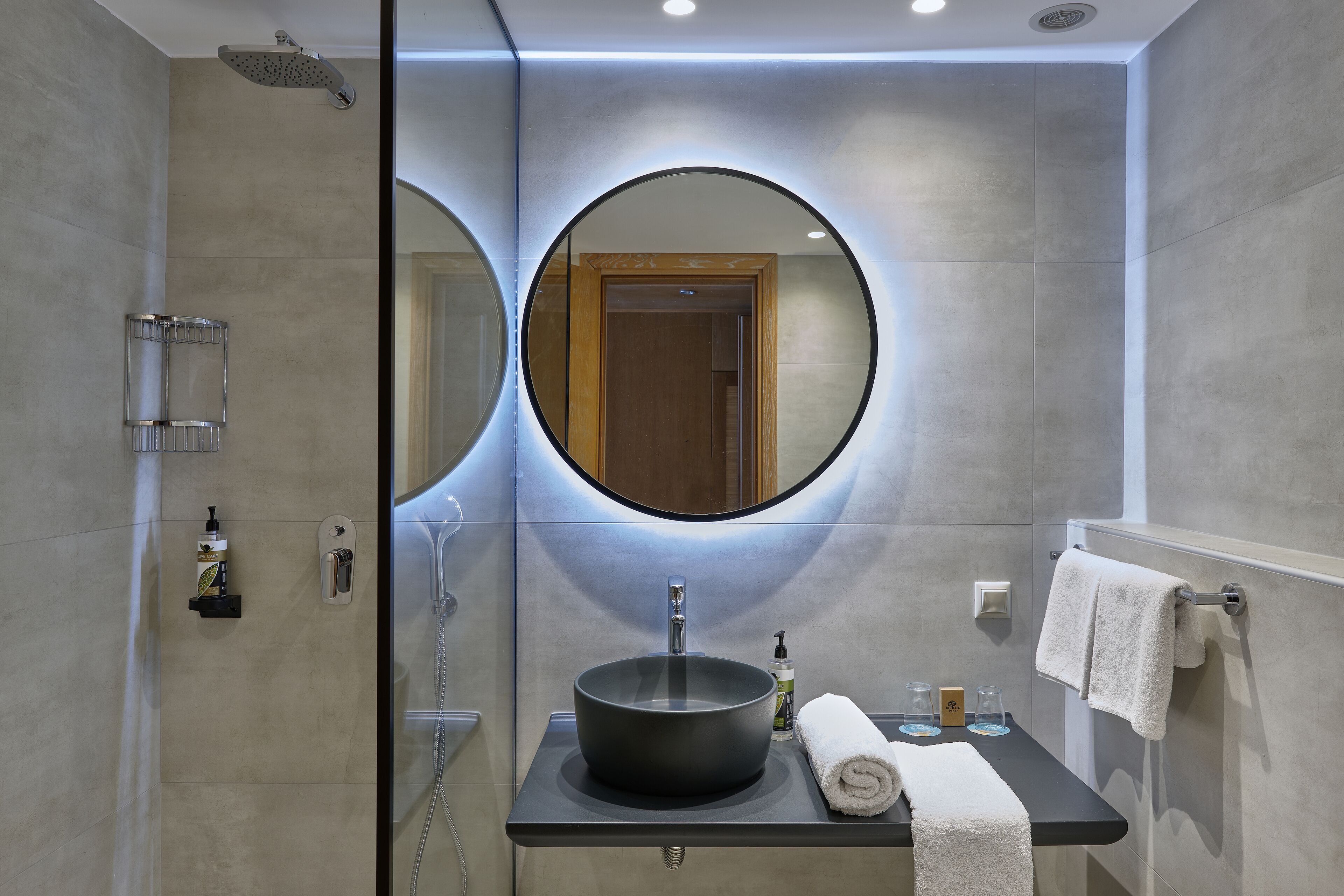 A modern bathroom with a round mirror, a black sink, and a towel rack.