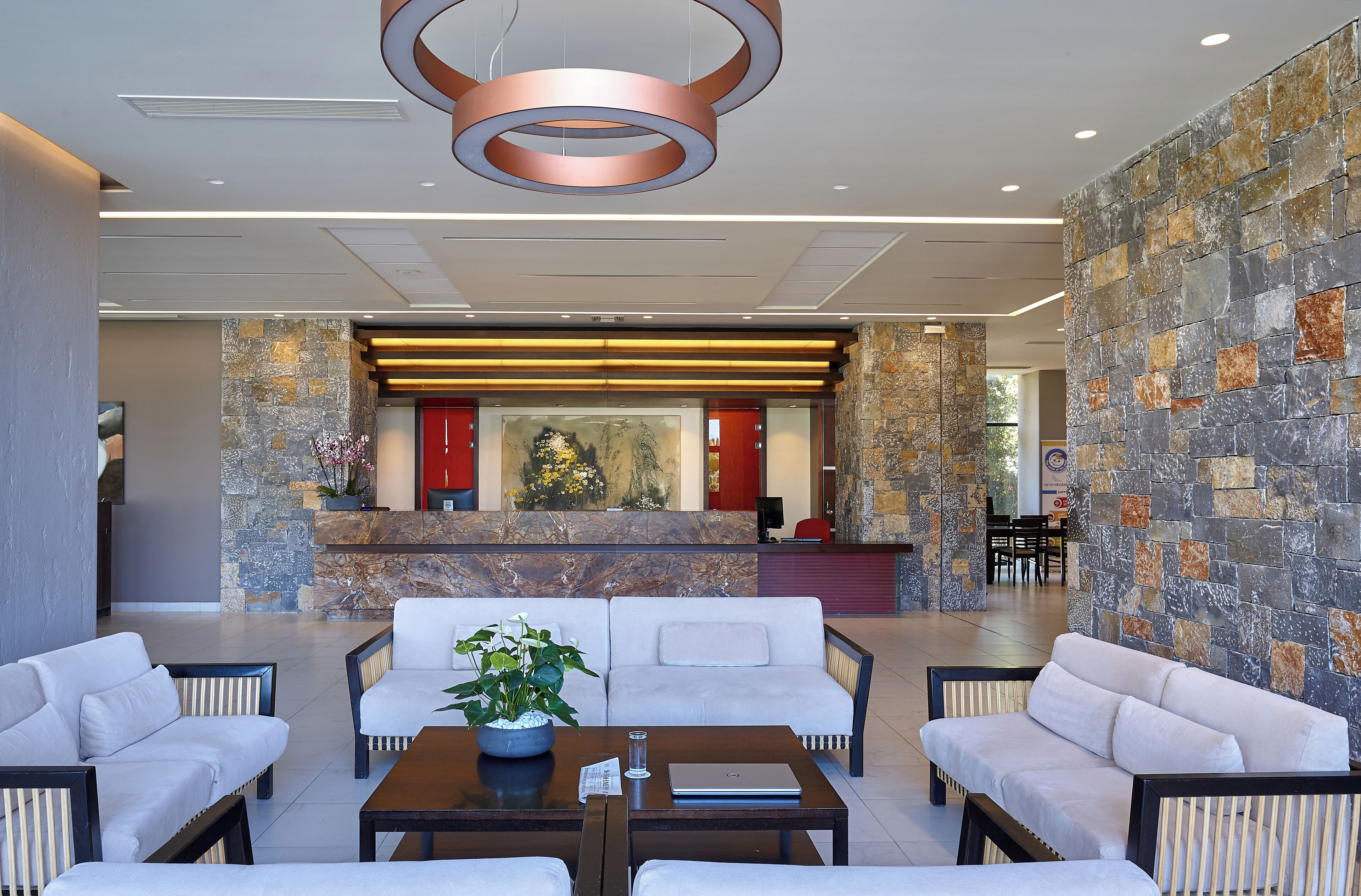 A spacious lobby with a reception desk, seating area, and a large painting.