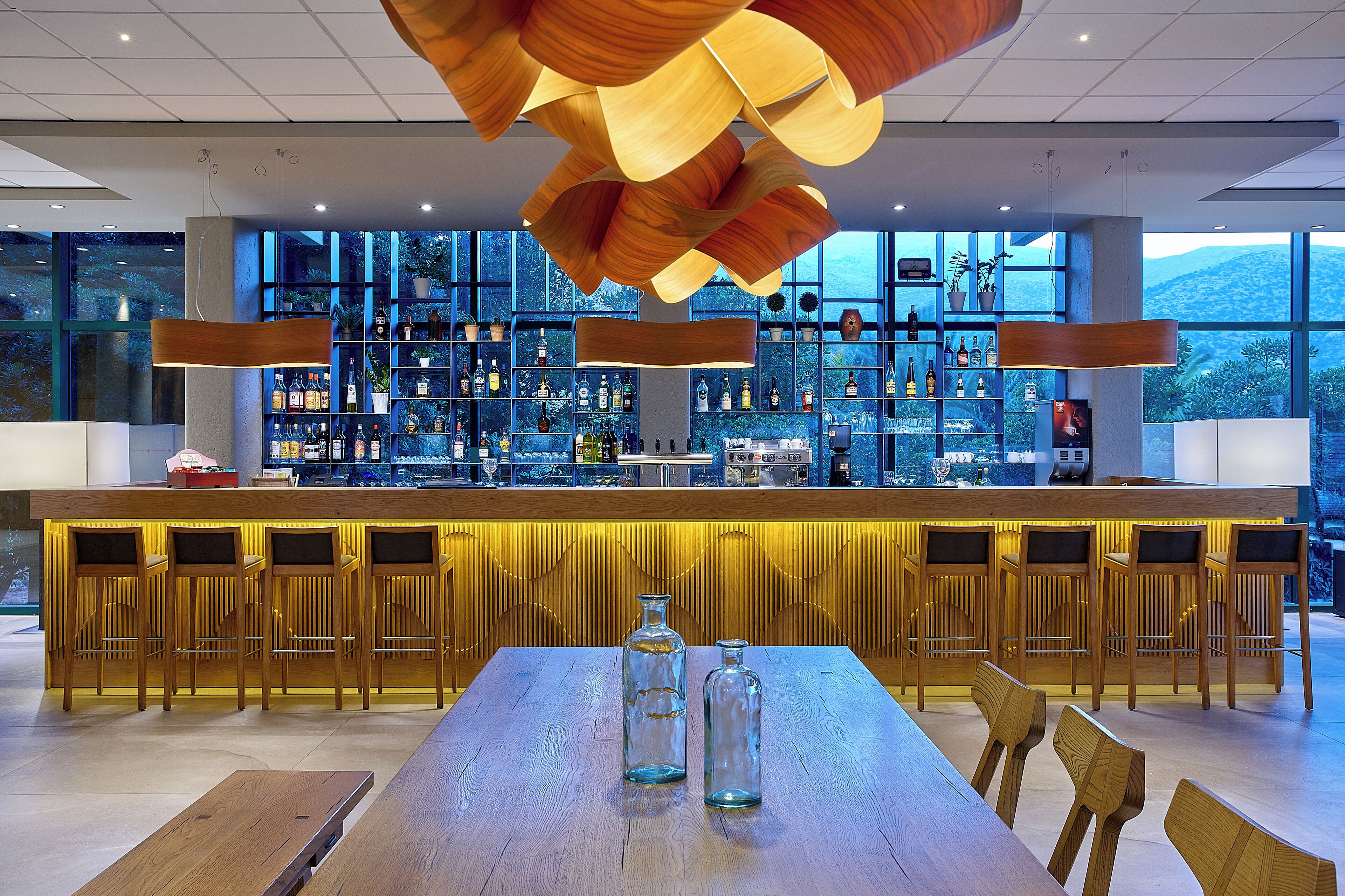 A modern bar area with a wooden bar counter, multiple seating options, and a view of the outdoors.