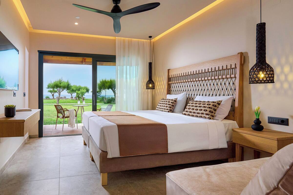 A modern bedroom with a large bed, a ceiling fan, and a view of the outdoors.