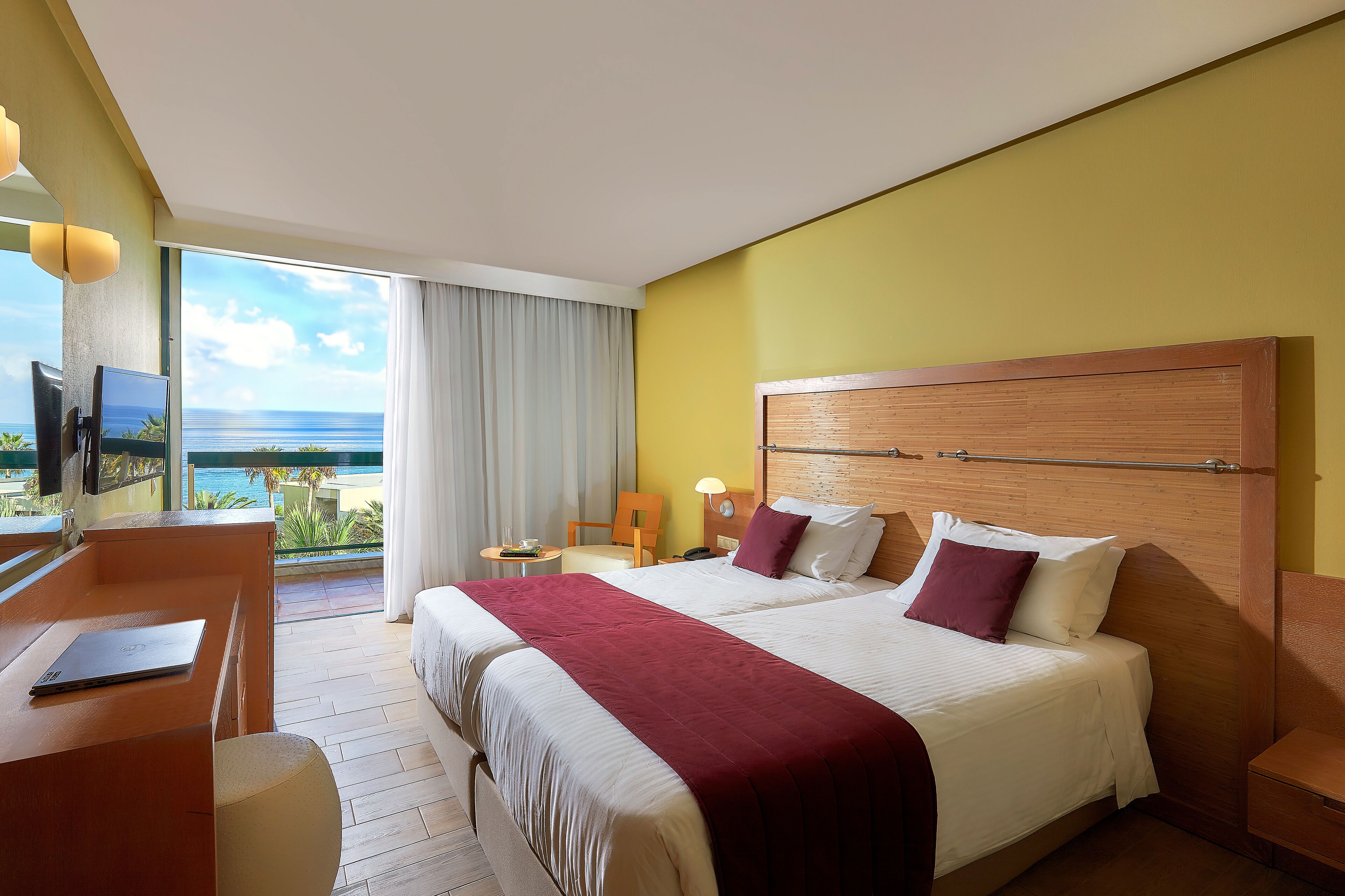 A hotel room with a large bed, a desk, a chair, and a view of the ocean.