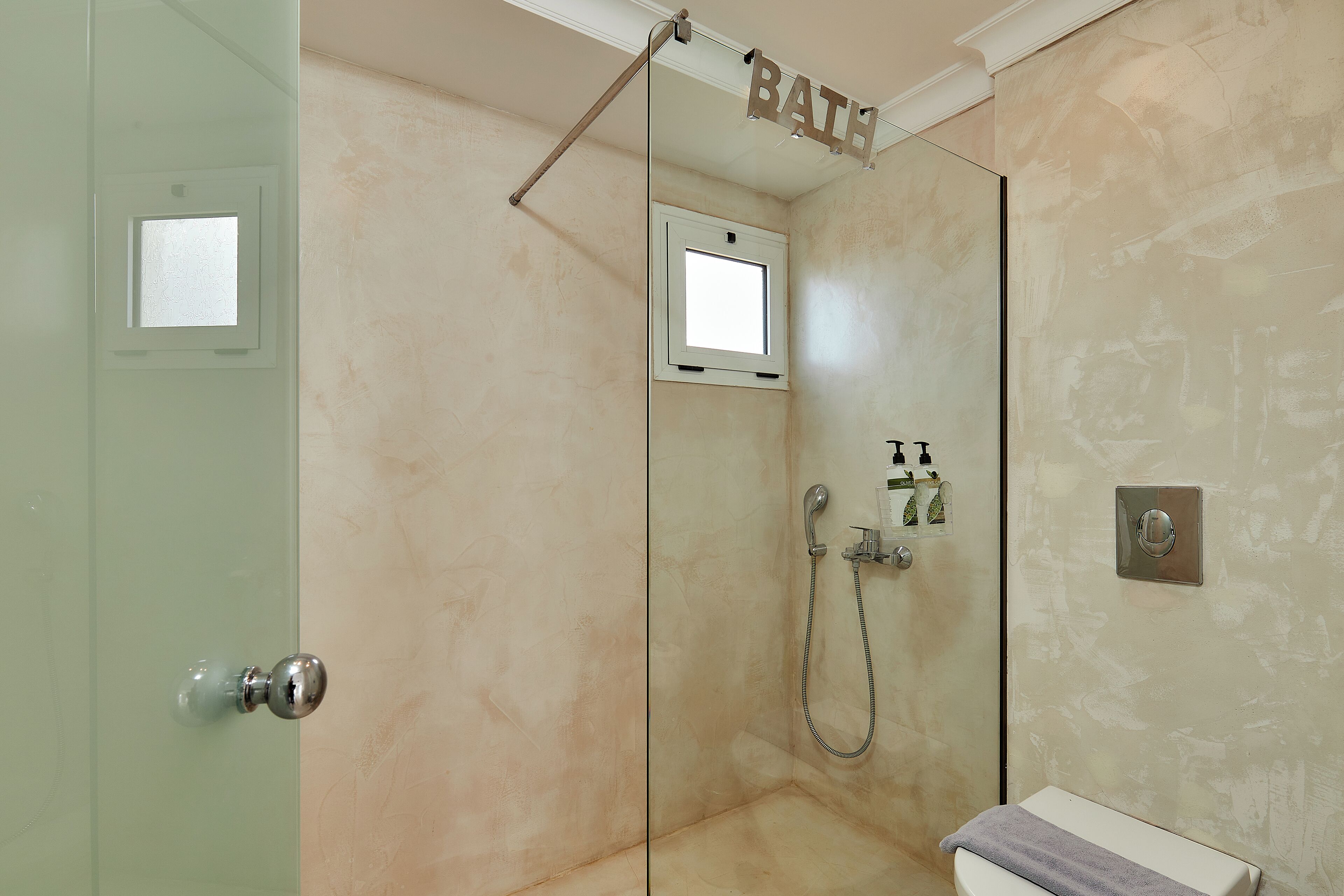 Un baño con puerta de cristal, ducha con cabezal de ducha manual, toallero y una ventana pequeña.