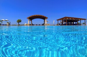 Una piscina azul cristalina con un arco de madera y una zona de estar cubierta.
