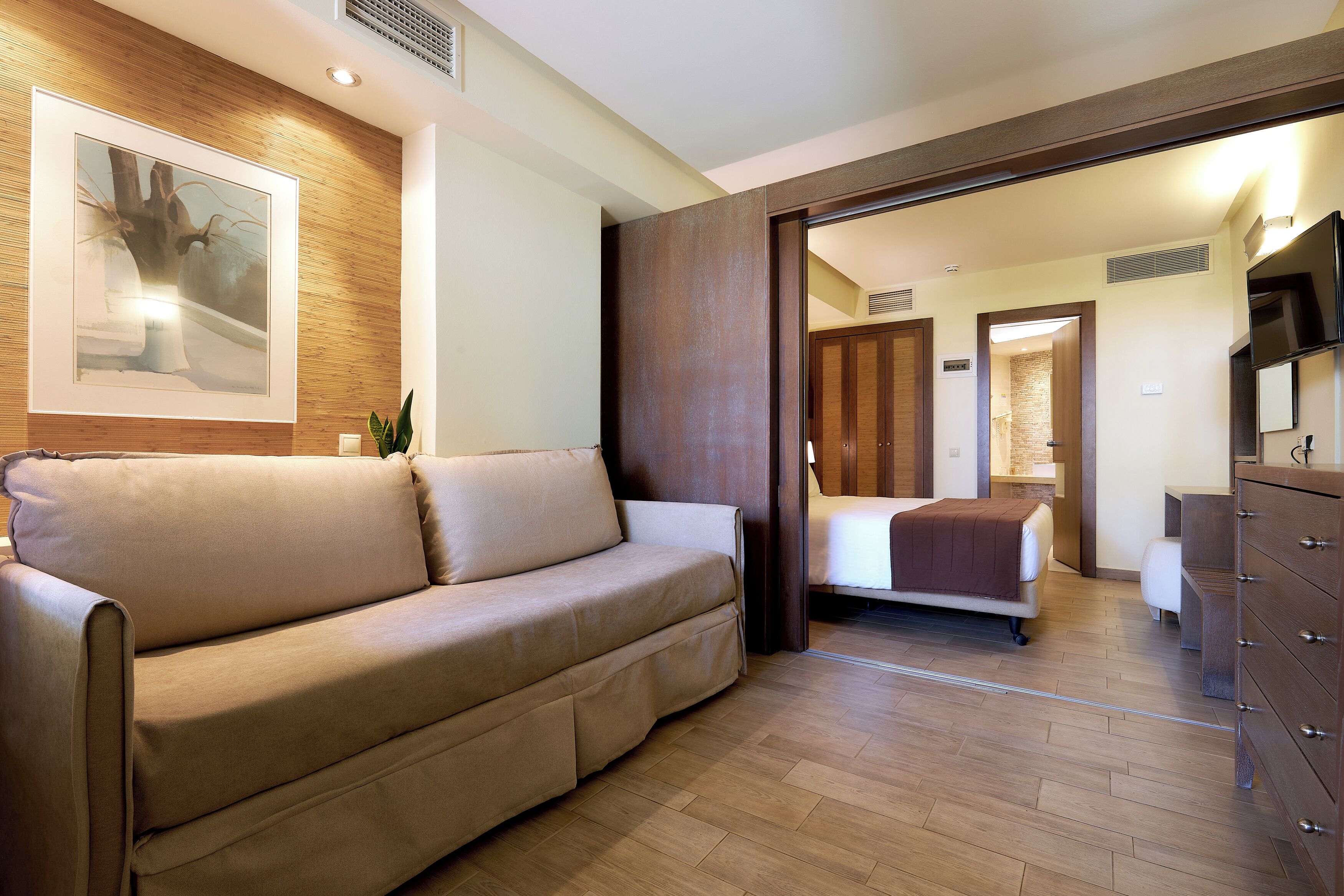 Una habitación de hotel con sofá, cama, cómoda y televisor.