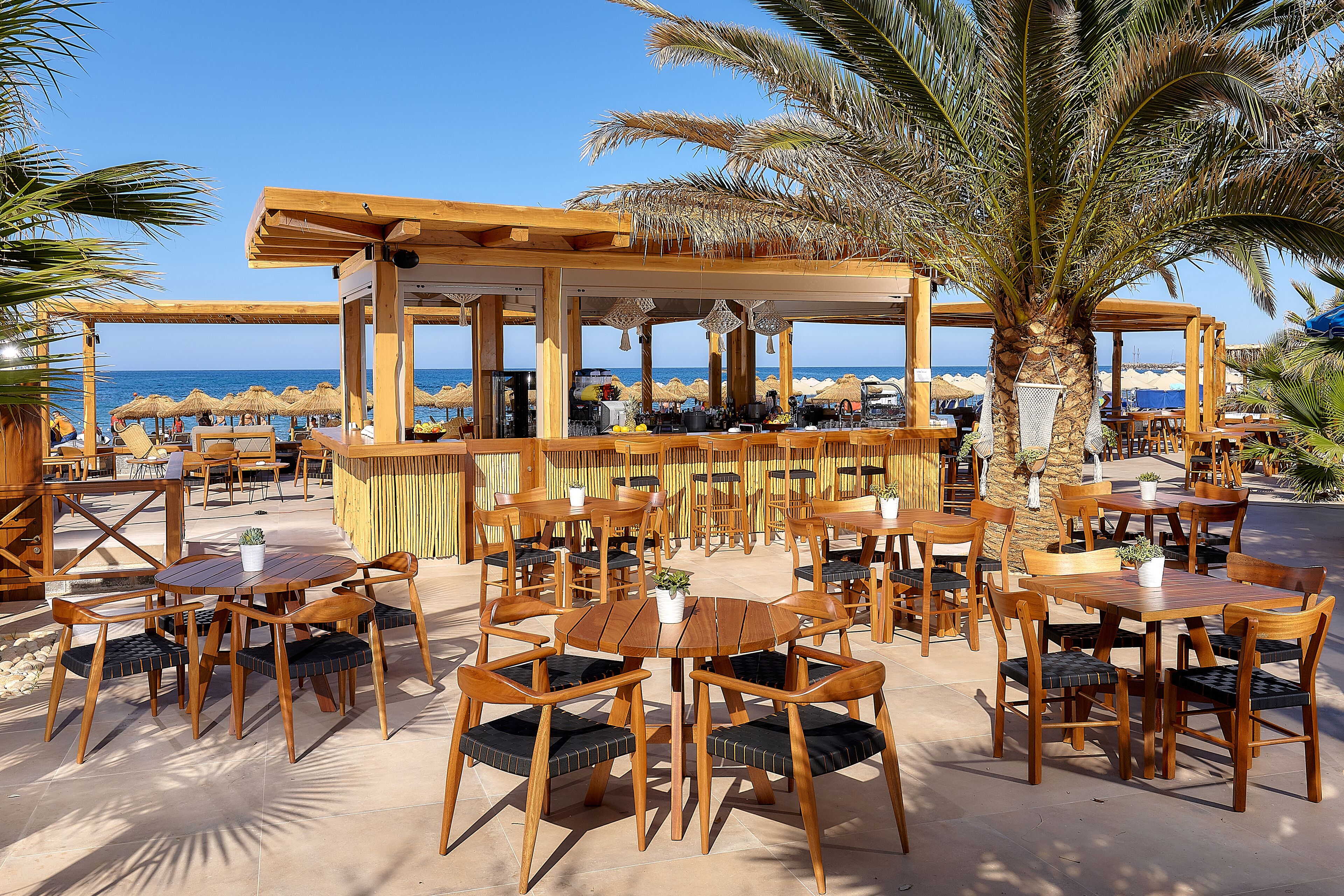 An outdoor seating area with wooden tables and chairs, a bar, and a view of the beach and ocean.
